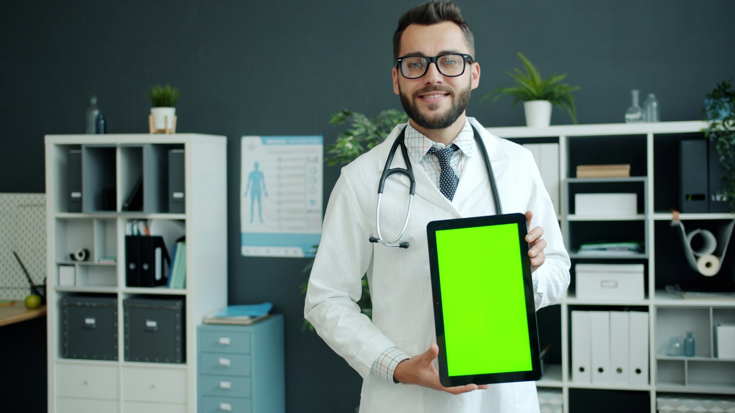 Doctor in a lab coat displays a tablet screen.
