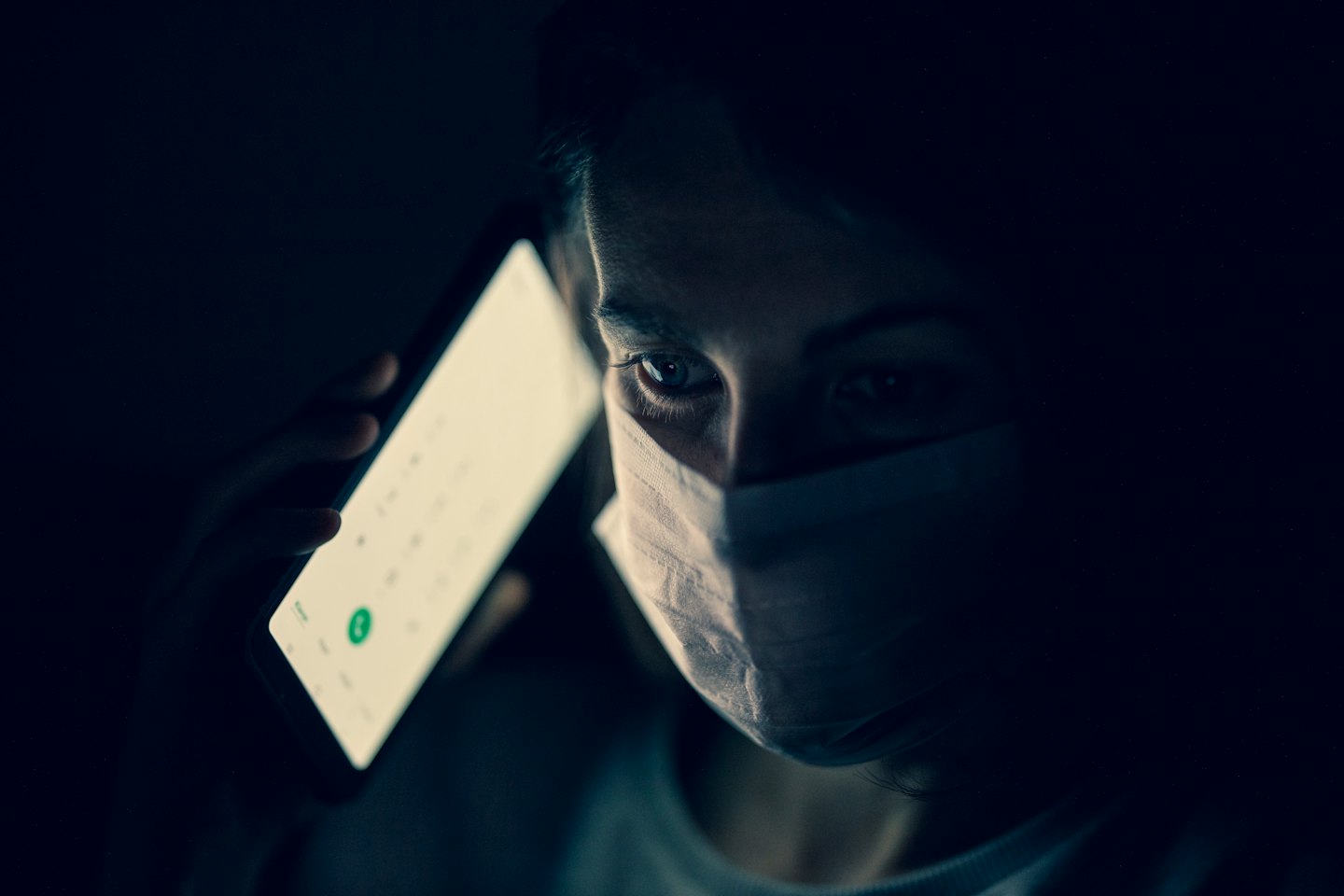Person wearing face mask talks on a glowing smartphone.