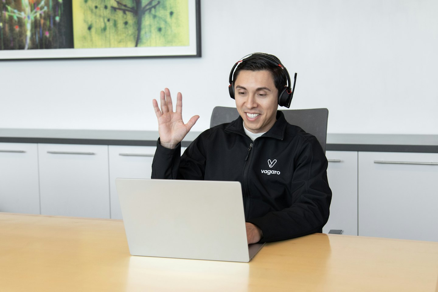Man with headphones smiles and waves during a video call.